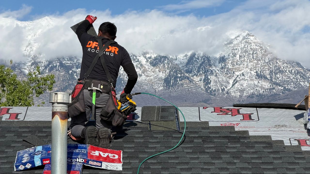 DFNDR roofer installing asphalt shingles on a Vineyard, Utah roof with snow-dusted Mount Timpanogos behind